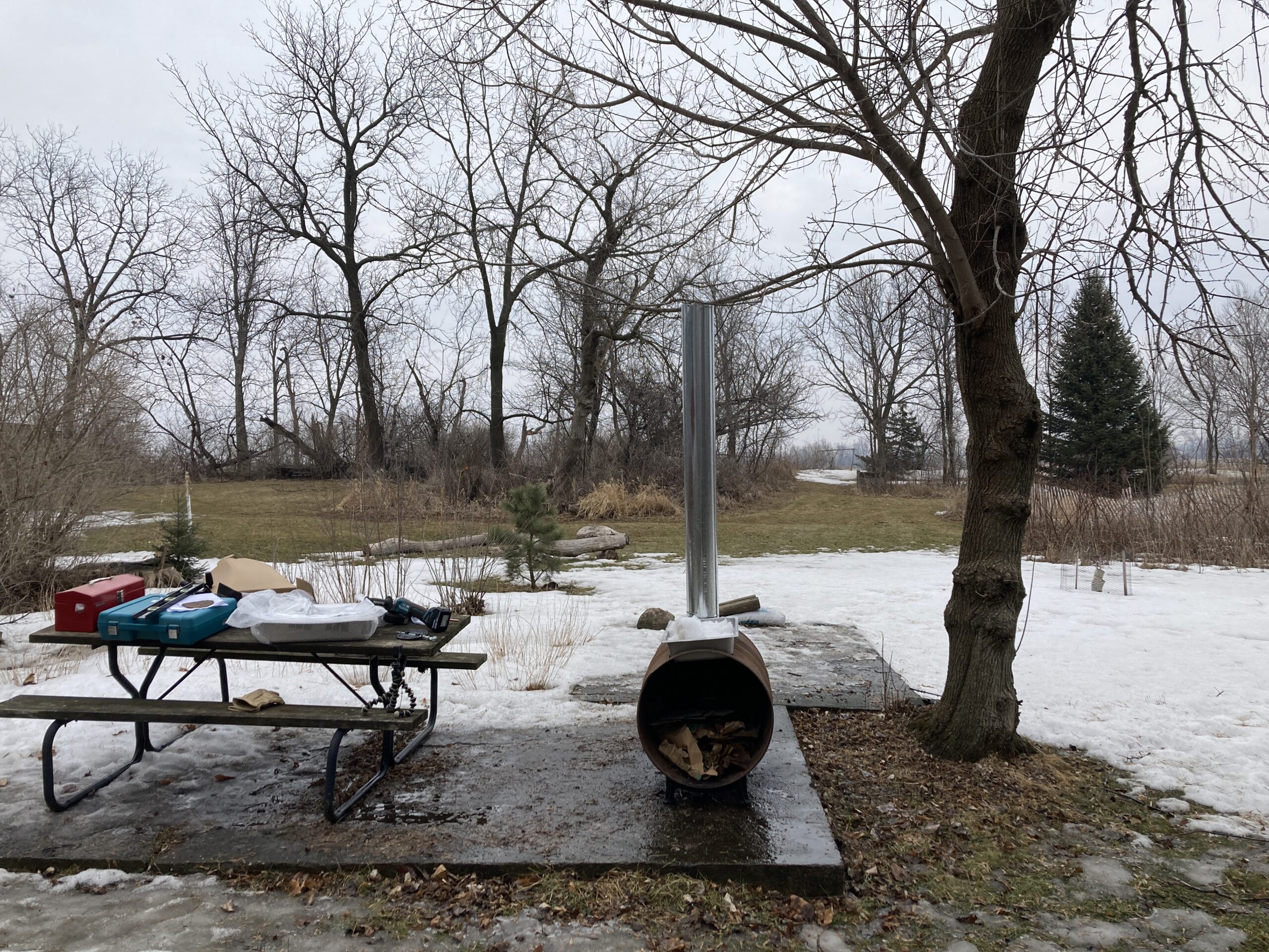 A homemade maple syrup evaporator sits on an old cement pad outside ready to make maple syrup.