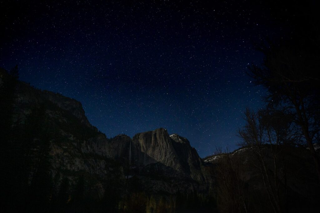 The view towards a very dark Yosemite Upper and Lower Falls from Swinging Bridge, on a dark night with the only illumination a nearly full moon lighting the mountains after dark.